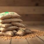 Consommation de pellets pour une maison de 80m2 : combien de sacs par an ? Pile de sacs en jute remplis de graines sur un parquet en bois